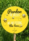 Yellow round sign with bees and the wording 'Pardon the weeds, we are feeding the bees'